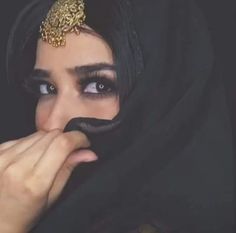 a woman wearing a black veil and gold head piece with her eyes wide open while covering her mouth