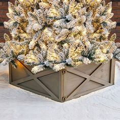 a christmas tree in a wooden box with snow on the top and bottom, next to a brick wall