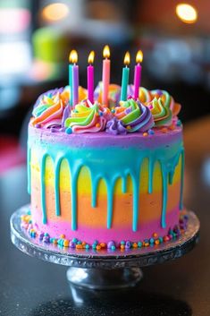 a birthday cake with multicolored icing and lit candles on top, sitting on a table