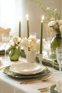 the table is set with white flowers and green plates, silverware, and candles