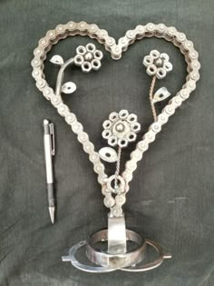 a heart shaped metal object with flowers on it and a pen next to it in the shape of a flower