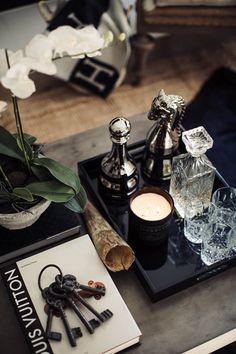 an assortment of bottles and keys on a tray next to a vase with flowers in it