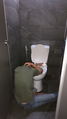 a man sitting on the toilet in a stall with his legs up and head down