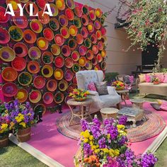 an outdoor area with flowers and chairs on the grass, surrounded by a wall made out of colorful plates