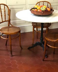 two wooden chairs sitting at a table with a bowl of fruit on top of it