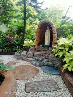 an outdoor garden with rocks, plants and a statue in the entrance to a cave