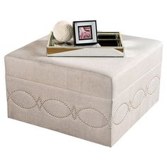 a white ottoman with an embroidered design on the top and bottom, sitting next to a photo frame