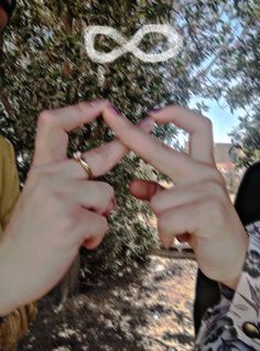 two people holding their hands together in the shape of an infinite sign with trees behind them