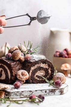 someone is sprinkling icing on a chocolate roll with cranberries and nuts