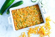 zucchini and cheese casserole in a white dish with cucumbers on the side