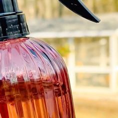 a close up of a red liquid bottle with a black cap on the top, and a white fence in the background