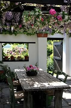 a wooden table sitting under a pergolia covered roof with flowers hanging from it