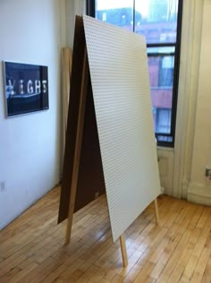 an easel sitting on top of a hard wood floor in front of a window