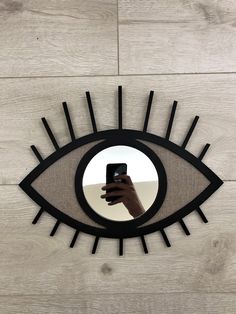 a hand holding a cell phone in front of an eye shaped mirror on the wall