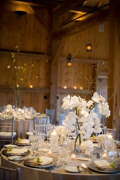 the tables are set with white flowers and candles for an elegant wedding reception in a barn