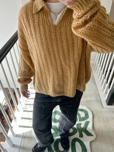 a little boy standing on the stairs with his hands in his ears and wearing a sweater