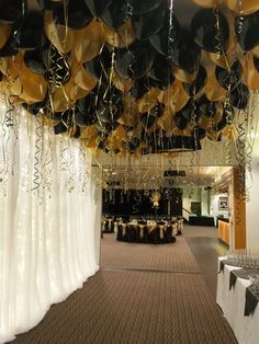 black and gold balloons hanging from the ceiling in a banquet hall with white drapes