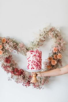 a person holding a cake with flowers on it in the shape of a heart and wreath