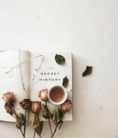 an open book with flowers and a cup of coffee sitting on the table next to it