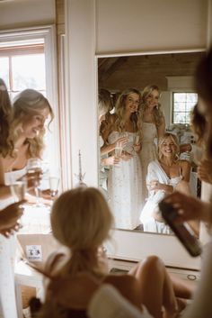 a group of women standing in front of a mirror holding wine glasses and looking at each other