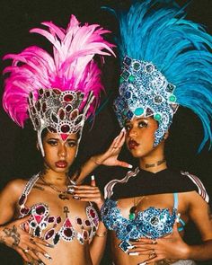 two women wearing colorful costumes and headdress standing next to each other in front of a black background