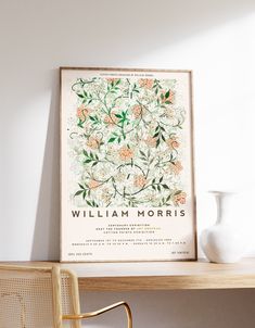 a white vase sitting on top of a wooden table next to a framed flower print