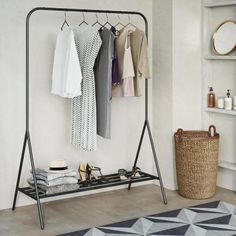 a rack with clothes hanging on it next to a rug in a room that is white and gray