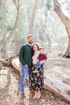 a man and woman pose for a family photo in the woods with their toddler