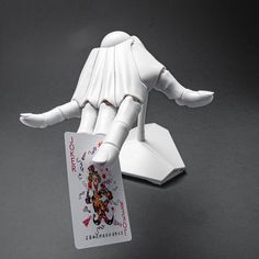 a white robot holding a playing card on top of a black table with gray background