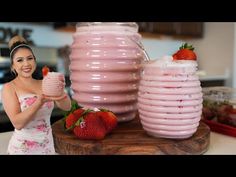 a woman in a dress is holding a drink and strawberries on the table next to two large pink vases