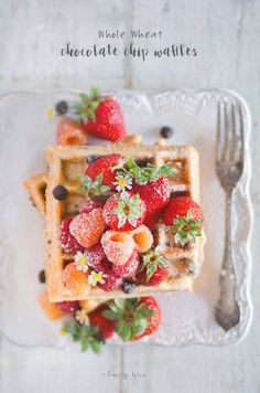 a plate with waffles, strawberries and chocolate chips on it next to a fork