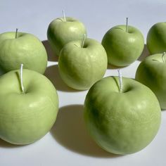 six green apples sitting on top of a white table next to each other with pins in them