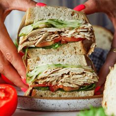 a person holding a sandwich in their hands with tomatoes and lettuce on the side