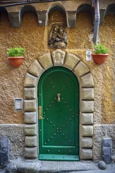 a green door in front of a stone building with potted plants on either side