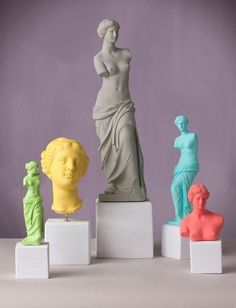 four different colored sculptures on pedestals in front of a purple wall, with one woman's head resting on her hand