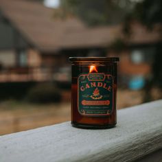 a candle sitting on top of a wooden ledge next to a house in the background