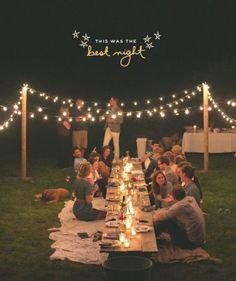 a group of people sitting around a long table with lights strung across the entire area