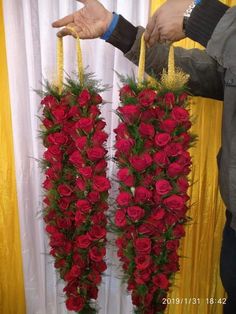 two people holding red roses in front of a white curtain with yellow drapes behind them