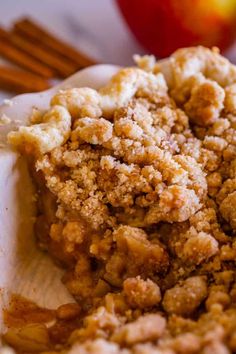 an apple pie with crumbs on top and cinnamon sticks in the back ground