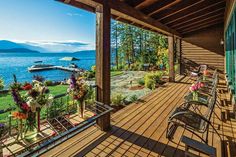 an outdoor deck with chairs and flowers on the grass next to it, overlooking a lake