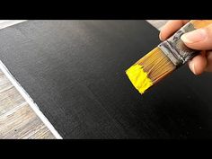 a person holding a paintbrush over a piece of black paper on a wooden floor