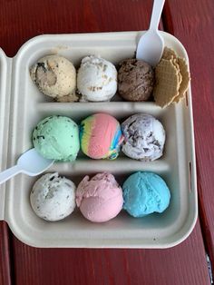 four scoops of ice cream in a tray on a wooden table with spoons