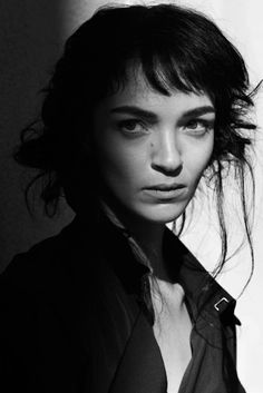 a black and white photo of a woman with her hair blowing in the wind, looking at the camera