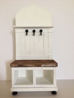 a white bench with two black hooks on it's back and some shelves underneath