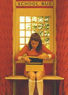 a woman sitting on a bench using a laptop computer in front of a school bus window