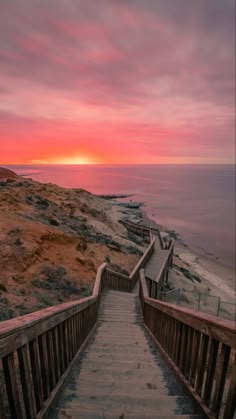 stairs leading down to the beach at sunset with pink and orange clouds in the background