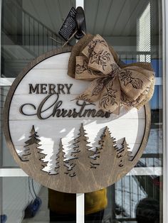 a merry christmas sign hanging from the side of a window with pine trees on it