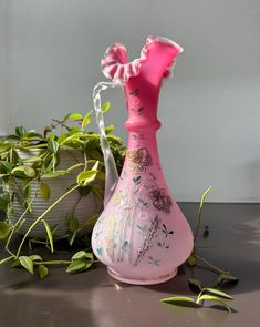 a pink vase sitting on top of a table next to a potted green plant