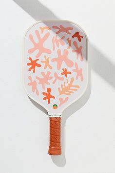 an orange and white paddle with coral designs on the side, against a white wall