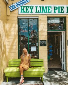 a woman sitting on a green bench in front of a coffee shop